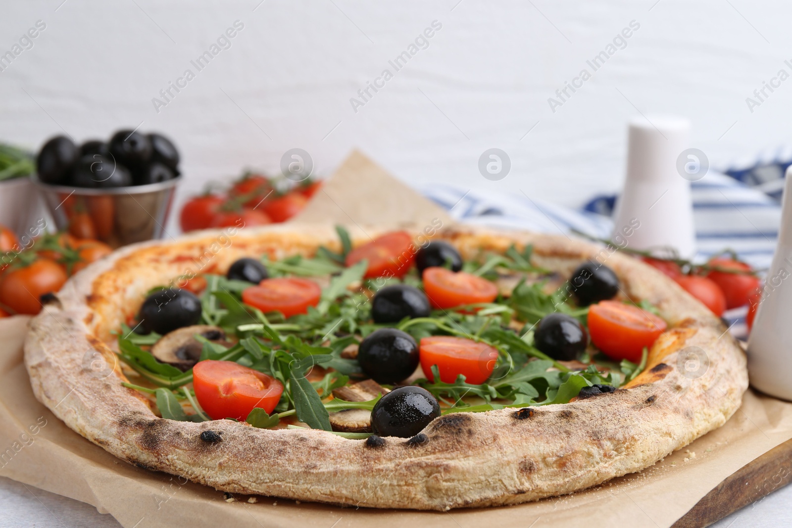 Photo of Tasty pizza with cherry tomatoes, black olives, mushrooms and arugula on white table, closeup