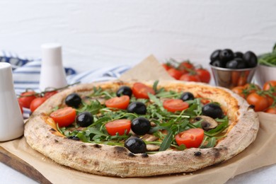 Photo of Tasty pizza with cherry tomatoes, black olives, mushrooms and arugula on white table, closeup