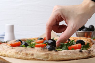 Photo of Woman putting black olive onto tasty pizza at table, closeup