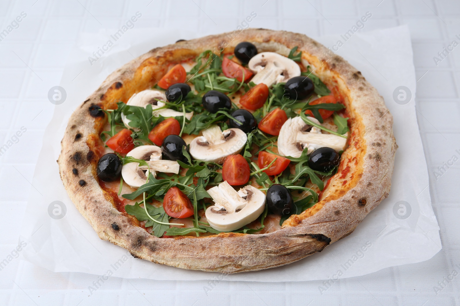 Tasty pizza with cherry tomatoes, black olives, mushrooms and arugula on white tiled table Photo of Tasty pizza with cherry tomatoes, black olives, mushrooms and arugula on white tiled table