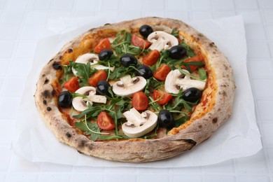 Photo of Tasty pizza with cherry tomatoes, black olives, mushrooms and arugula on white tiled table