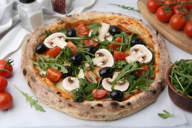 Photo of Tasty pizza with cherry tomatoes, black olives, mushrooms and arugula on white table, closeup