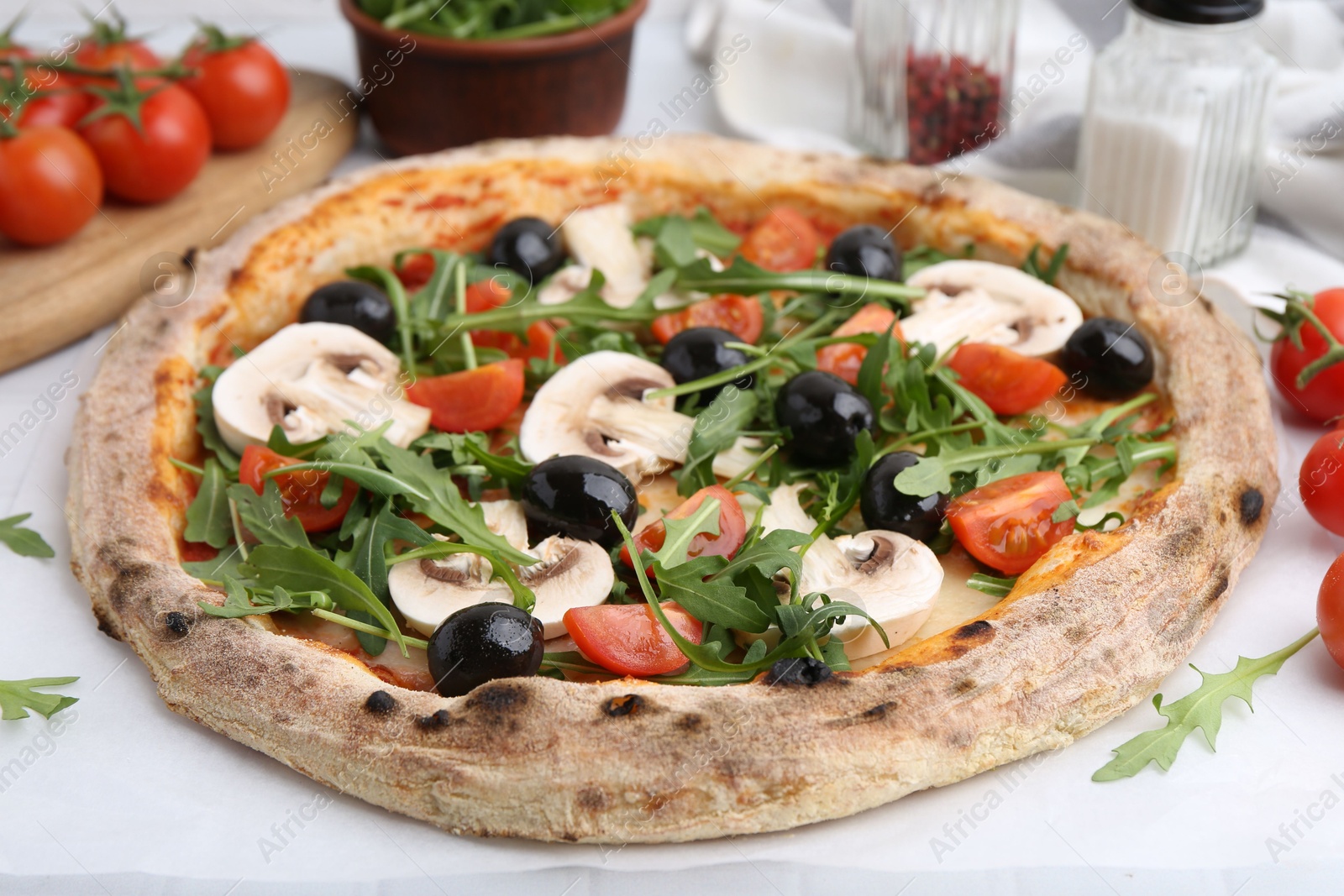Tasty pizza with cherry tomatoes, black olives, mushrooms and arugula on white table, closeup Photo of Tasty pizza with cherry tomatoes, black olives, mushrooms and arugula on white table, closeup