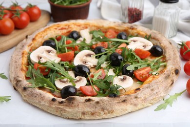 Photo of Tasty pizza with cherry tomatoes, black olives, mushrooms and arugula on white table, closeup