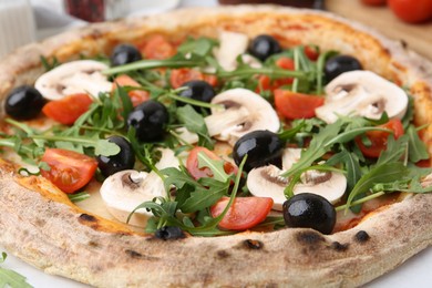 Photo of Tasty pizza with cherry tomatoes, black olives, mushrooms and arugula on white table, closeup