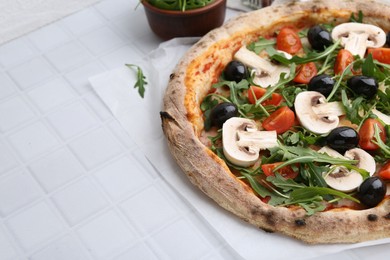 Photo of Tasty pizza with cherry tomatoes, black olives, mushrooms and arugula on white tiled table, closeup. Space for text