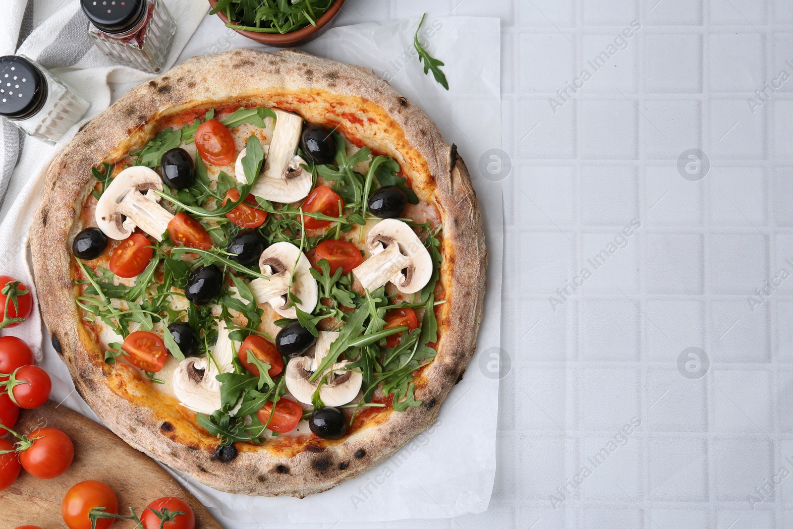 Tasty pizza with cherry tomatoes, black olives, mushrooms and arugula on white tiled table, flat lay. Space for text Photo of Tasty pizza with cherry tomatoes, black olives, mushrooms and arugula on white tiled table, flat lay. Space for text
