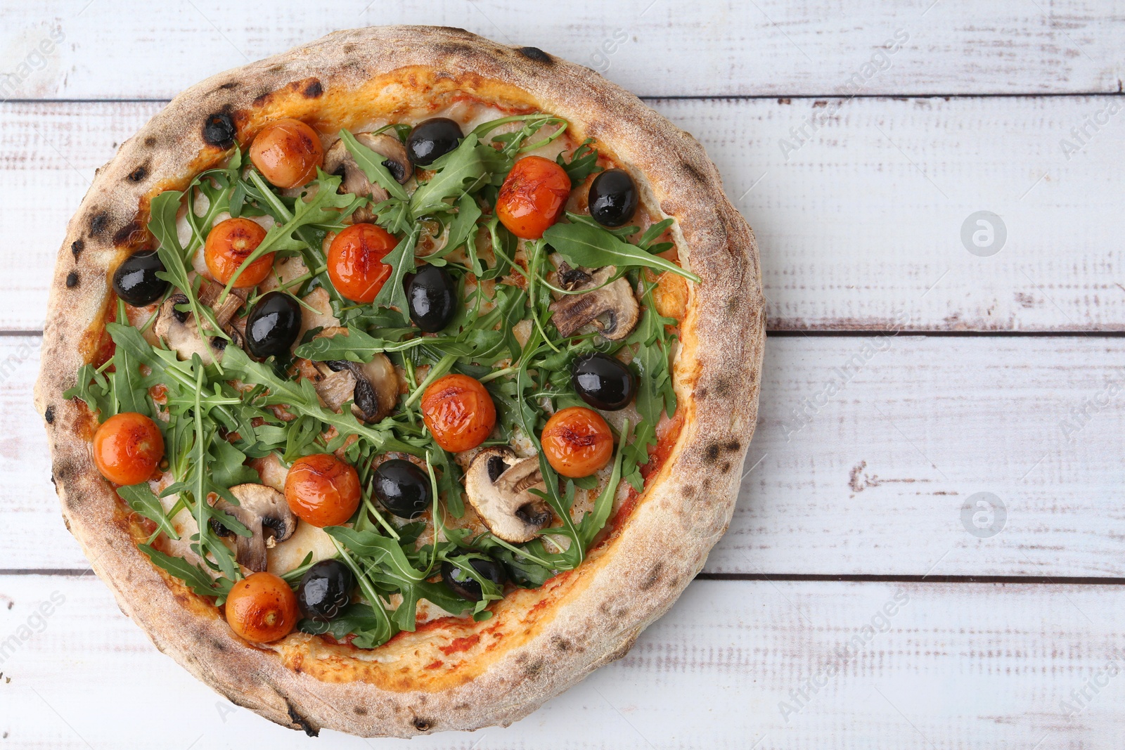 Tasty pizza with cherry tomatoes, black olives, mushrooms and arugula on white wooden table, top view. Space for text Photo of Tasty pizza with cherry tomatoes, black olives, mushrooms and arugula on white wooden table, top view. Space for text