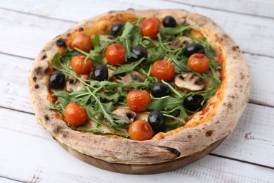 Photo of Tasty pizza with cherry tomatoes, black olives, mushrooms and arugula on white wooden table