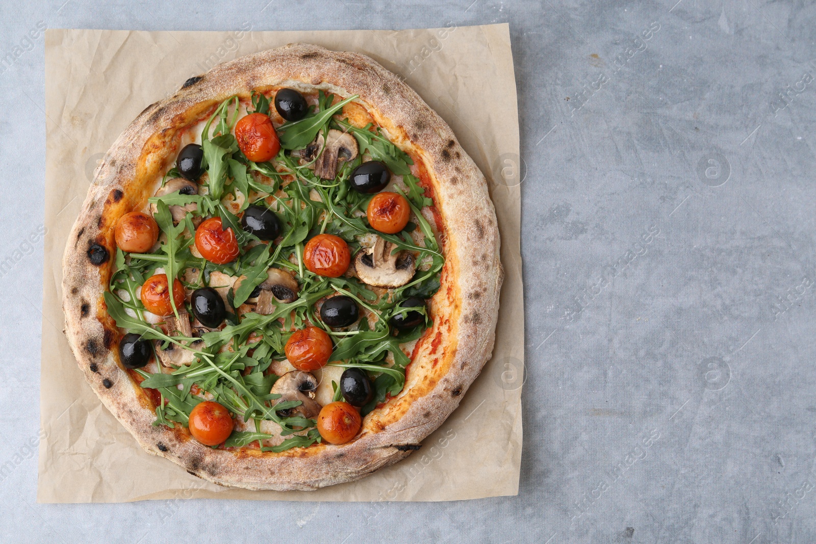 Tasty pizza with cherry tomatoes, black olives, mushrooms and arugula on grey table, top view. Space for text Photo of Tasty pizza with cherry tomatoes, black olives, mushrooms and arugula on grey table, top view. Space for text