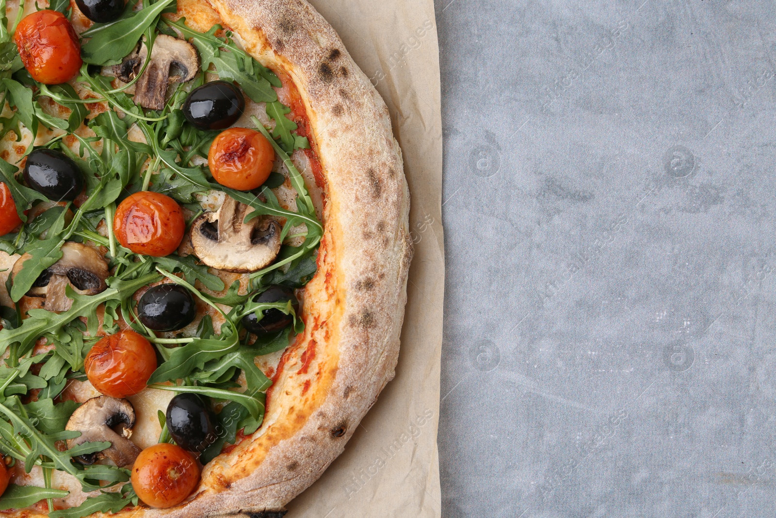 Tasty pizza with cherry tomatoes, black olives, mushrooms and arugula on grey table, top view. Space for text Photo of Tasty pizza with cherry tomatoes, black olives, mushrooms and arugula on grey table, top view. Space for text