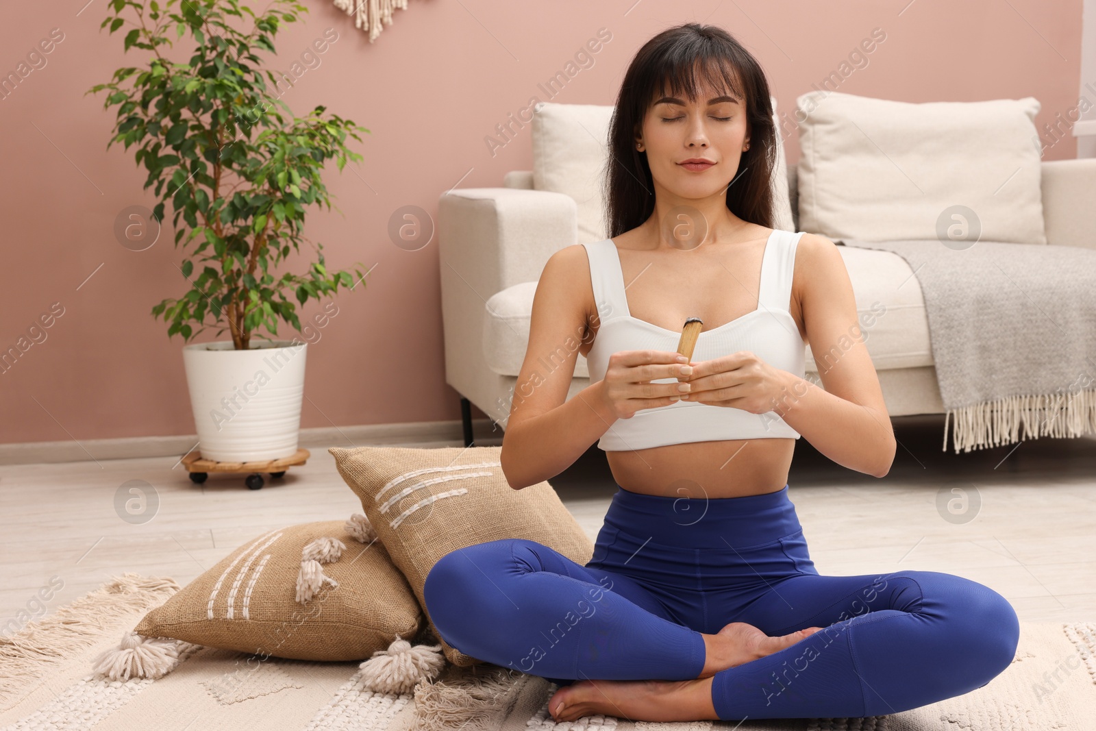 Photo of Woman with smoldering palo santo stick on floor at home