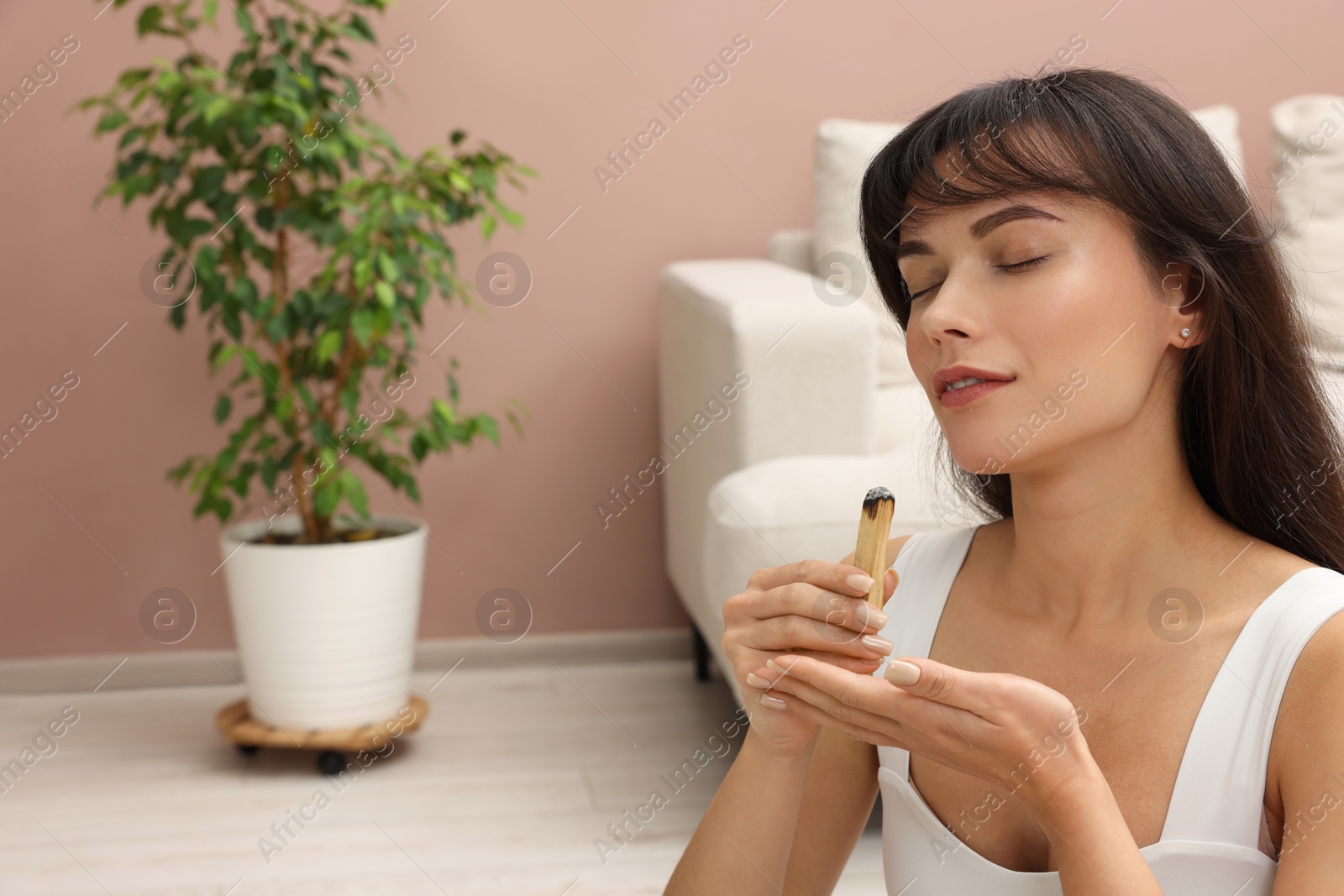 Photo of Woman with smoldering palo santo stick at home, space for text