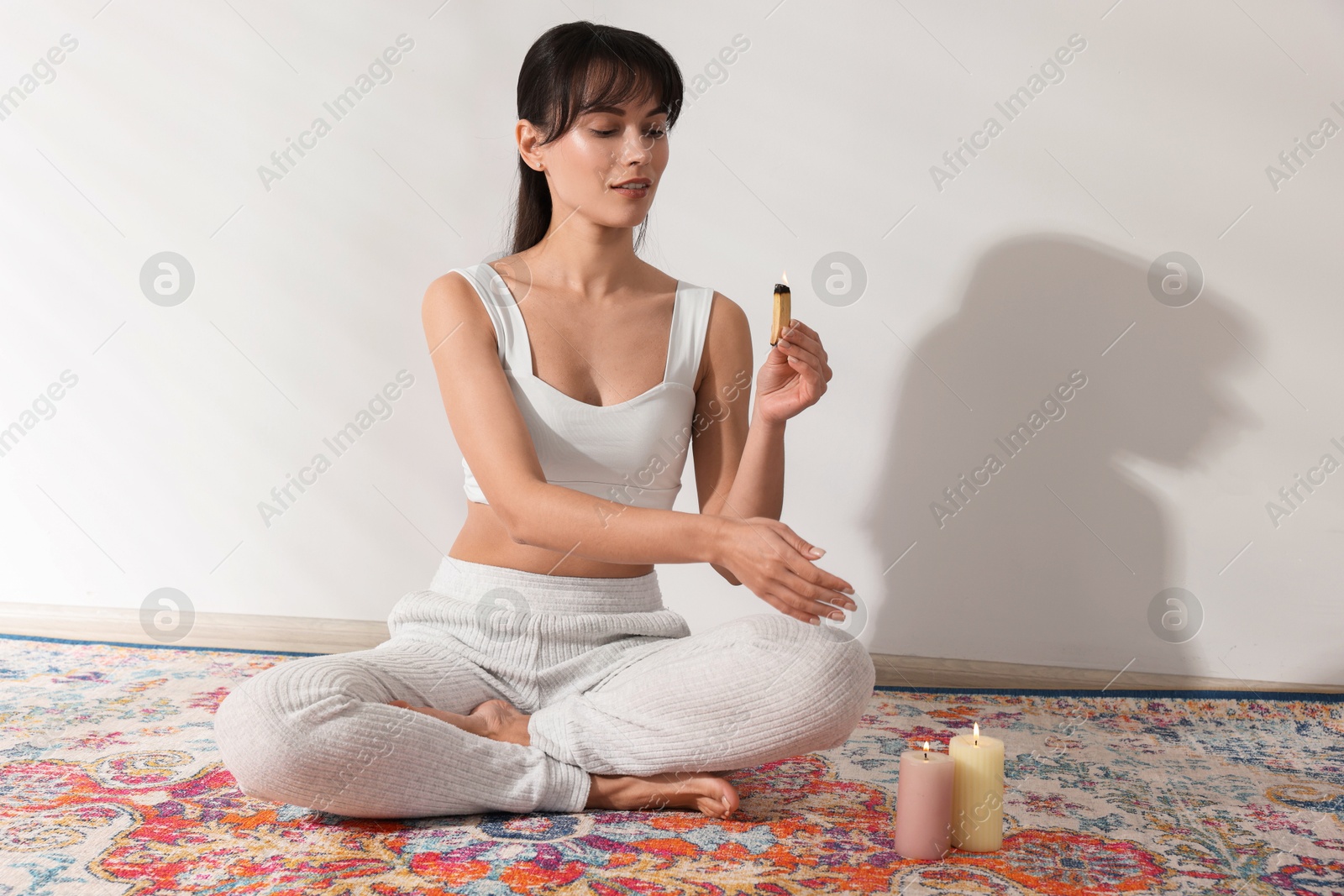 Photo of Woman with burning palo santo stick on floor at home, space for text