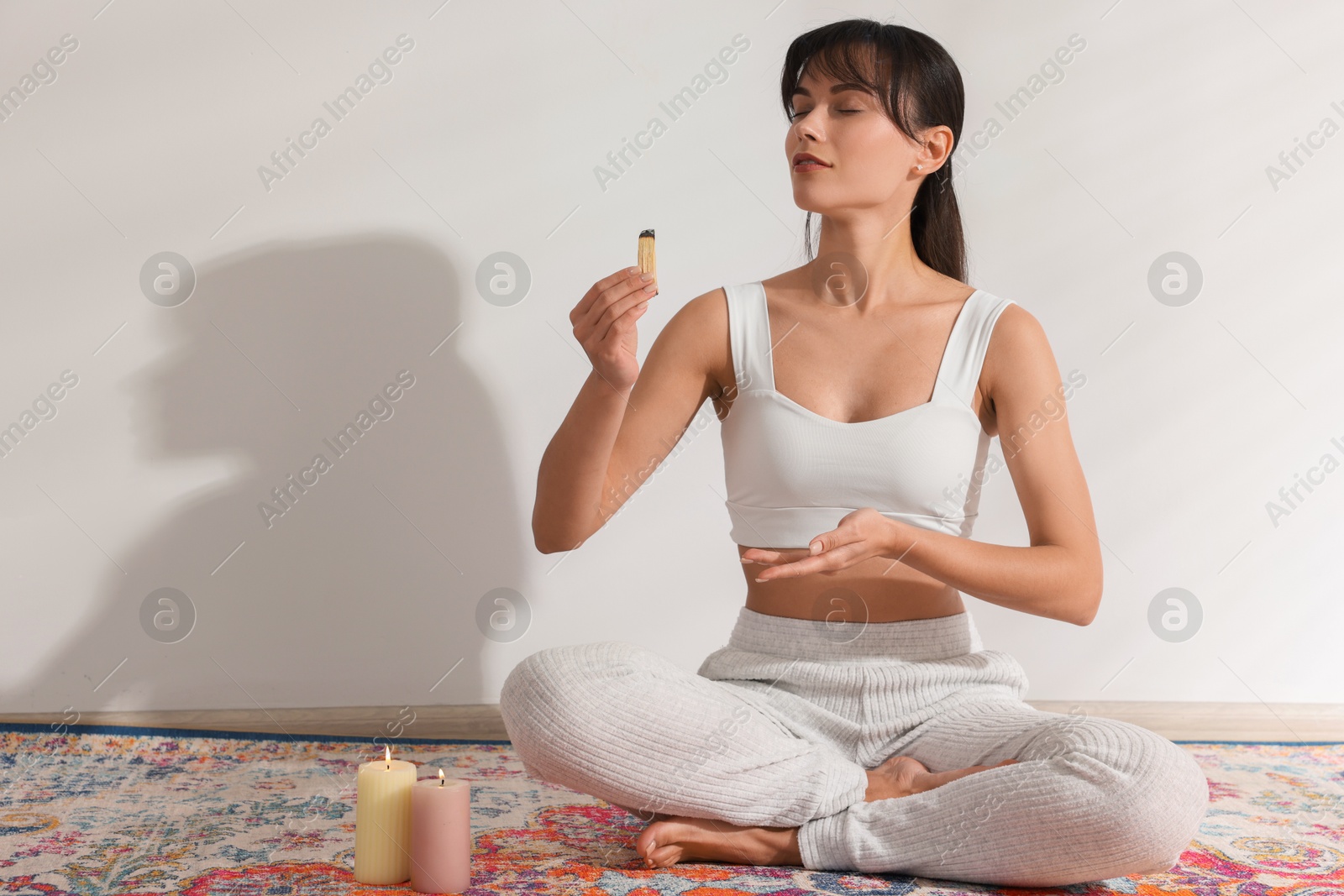 Photo of Woman with smoldering palo santo stick on floor at home, space for text