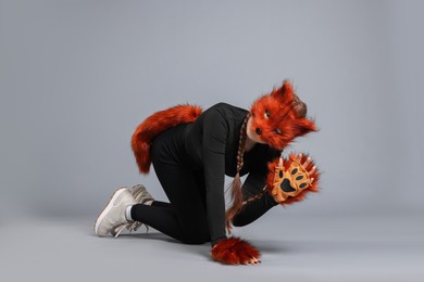 Photo of Quadrobics. Girl wearing fox mask, gloves and tail on grey background