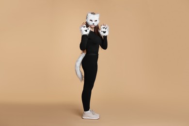 Photo of Quadrobics. Girl wearing cat mask, gloves and tail on beige background