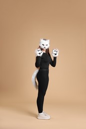 Photo of Quadrobics. Girl wearing cat mask, gloves and tail on beige background