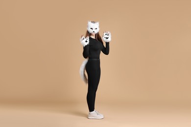 Photo of Quadrobics. Girl wearing cat mask, gloves and tail on beige background