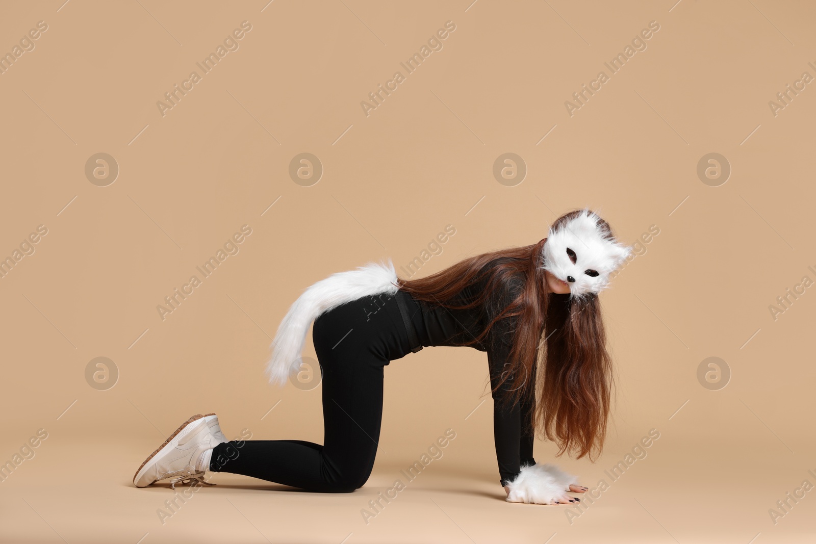 Photo of Quadrobics. Girl wearing cat mask, gloves and tail on beige background