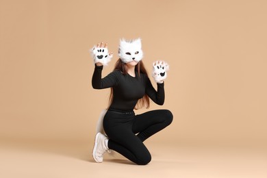 Photo of Quadrobics. Girl wearing cat mask, gloves and tail on beige background