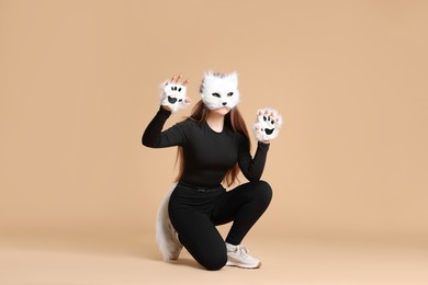 Photo of Quadrobics. Girl wearing cat mask, gloves and tail on beige background