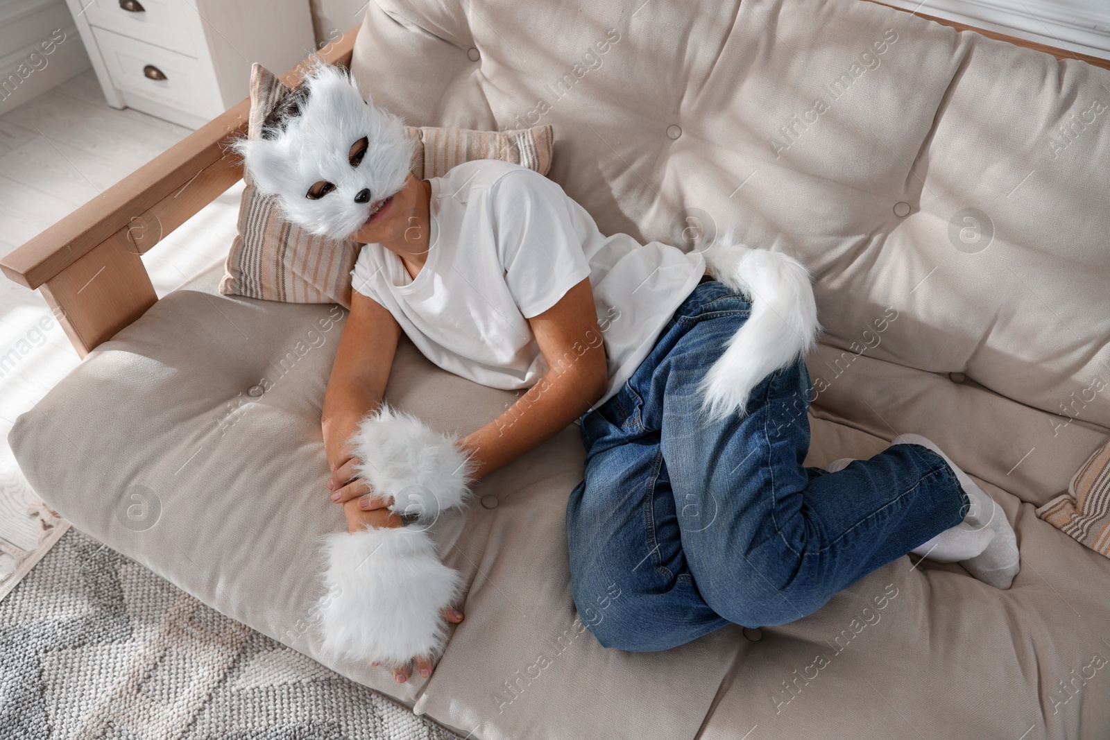 Photo of Quadrobics. Boy wearing cat mask, gloves and tail on sofa at home