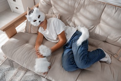 Photo of Quadrobics. Boy wearing cat mask, gloves and tail on sofa at home