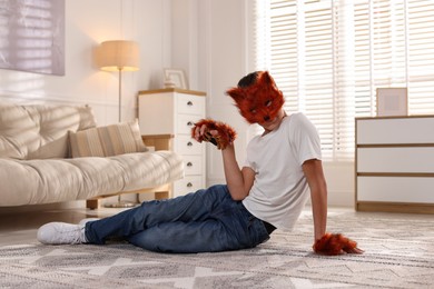 Photo of Quadrobics. Boy wearing fox mask and gloves on floor at home