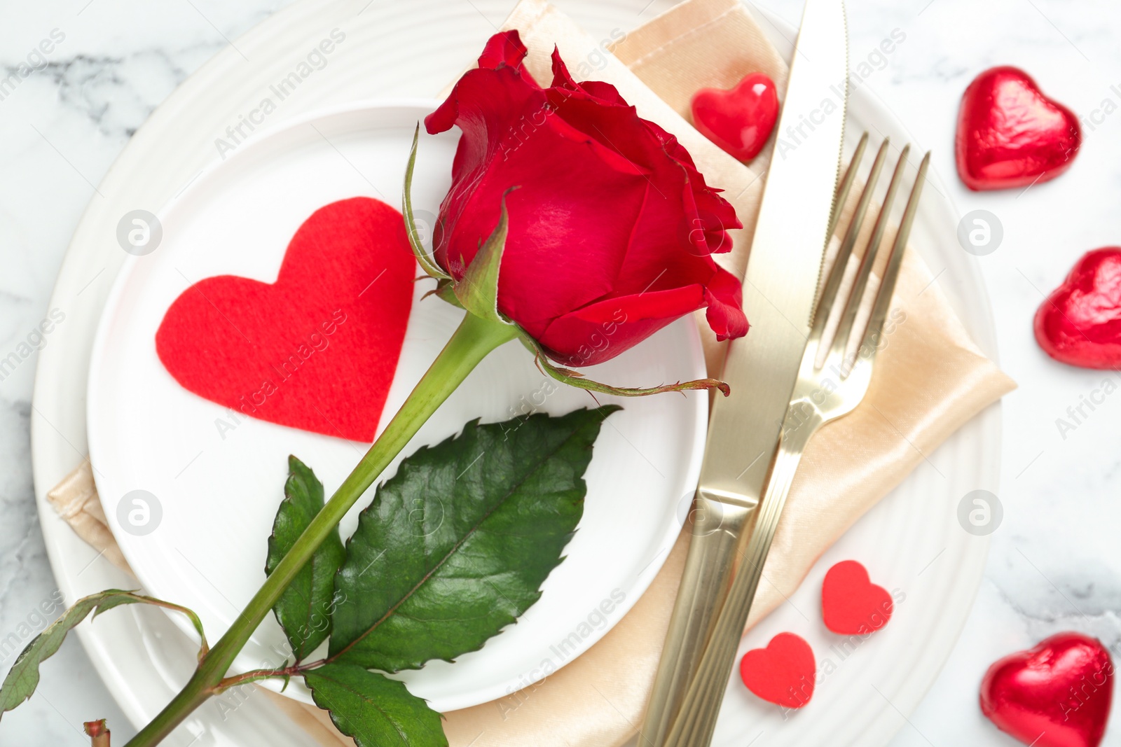 Photo of Romantic place setting for Valentine's day. Tableware, cutlery, rose and decorative hearts on white marble table, flat lay