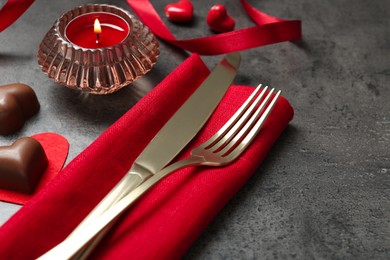 Photo of Romantic place setting for Valentine's day. Cutlery, candies, burning candle and decorative hearts on grey textured table, closeup