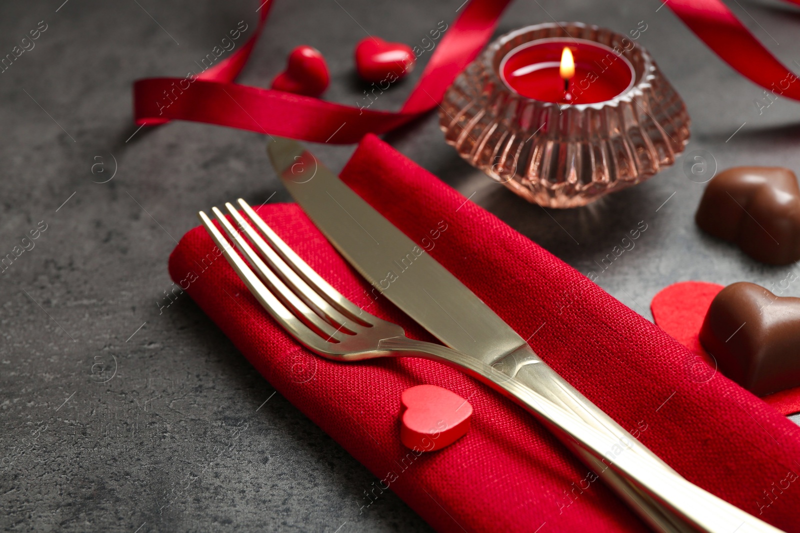 Photo of Romantic place setting for Valentine's day. Cutlery, candies, burning candle and decorative hearts on grey textured table, closeup