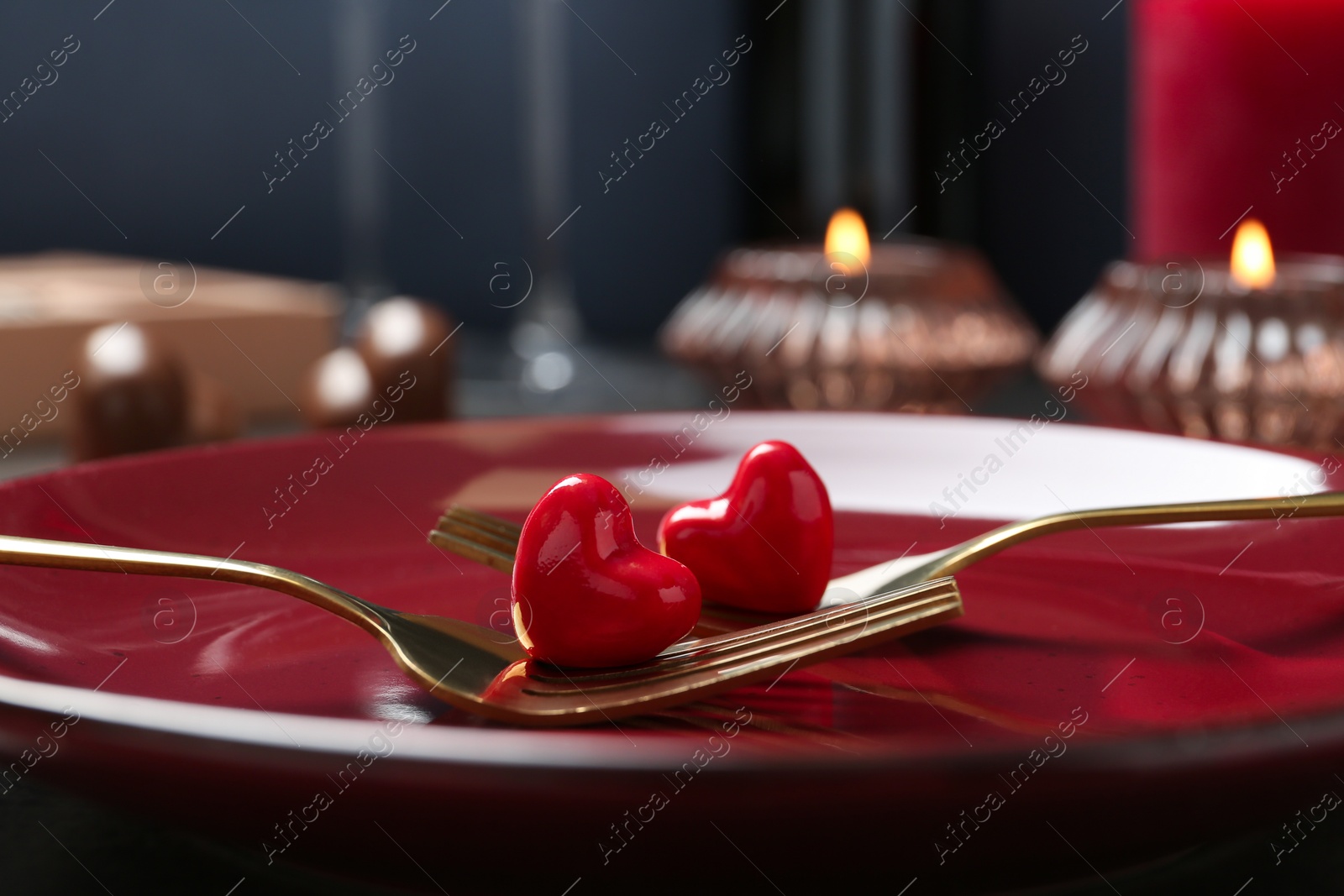 Photo of Romantic table setting for Valentine's day. Forks with decorative hearts on red plate, closeup