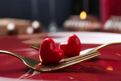 Photo of Romantic table setting for Valentine's day. Forks with decorative hearts on red plate, closeup