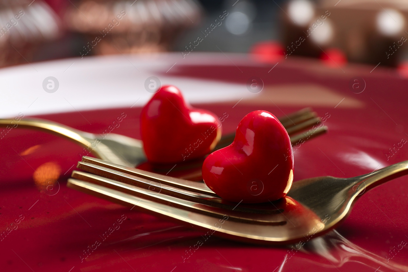 Photo of Romantic table setting for Valentine's day. Forks with decorative hearts on red plate, closeup