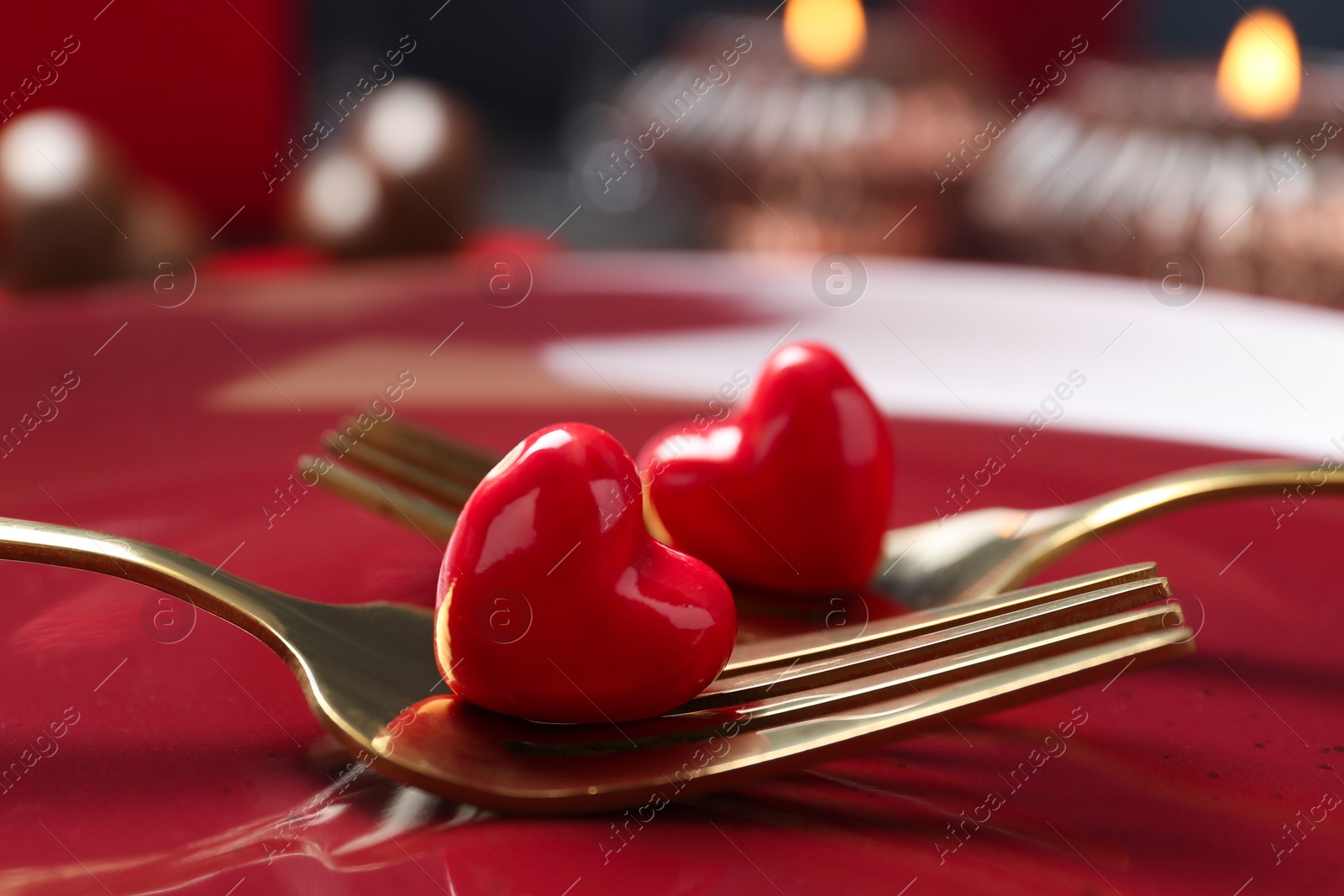 Photo of Romantic table setting for Valentine's day. Forks with decorative hearts on red plate, closeup