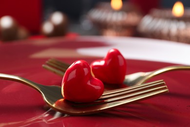 Photo of Romantic table setting for Valentine's day. Forks with decorative hearts on red plate, closeup