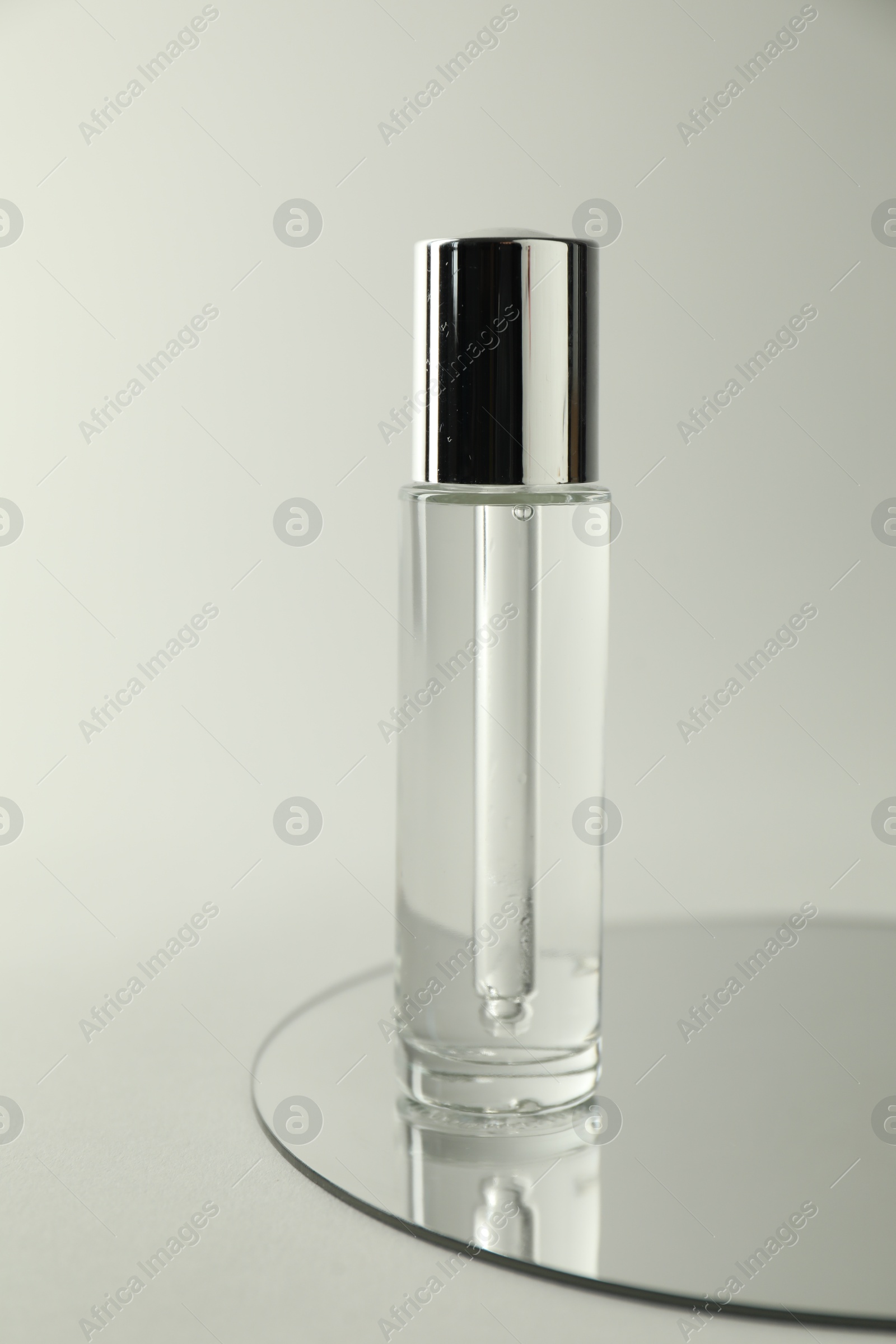 Photo of Bottle of serum and mirror on light background