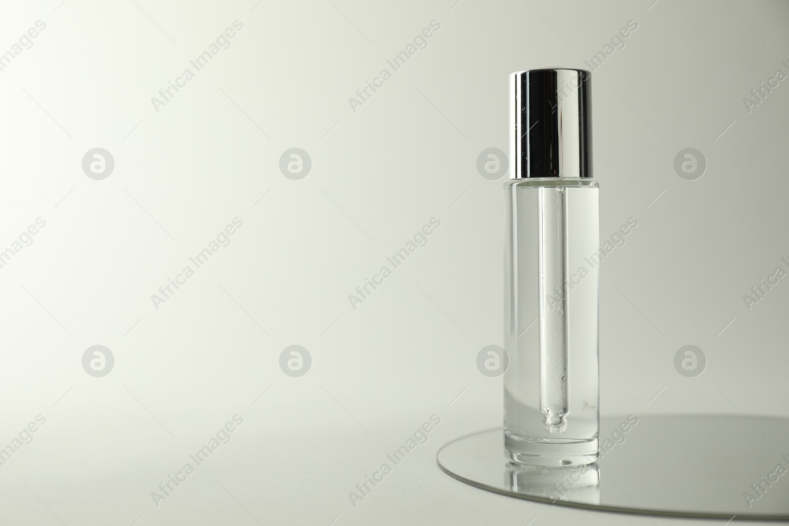 Photo of Bottle of serum and mirror on light background, space for text