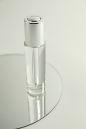 Photo of Bottle of serum and mirror on light background, closeup