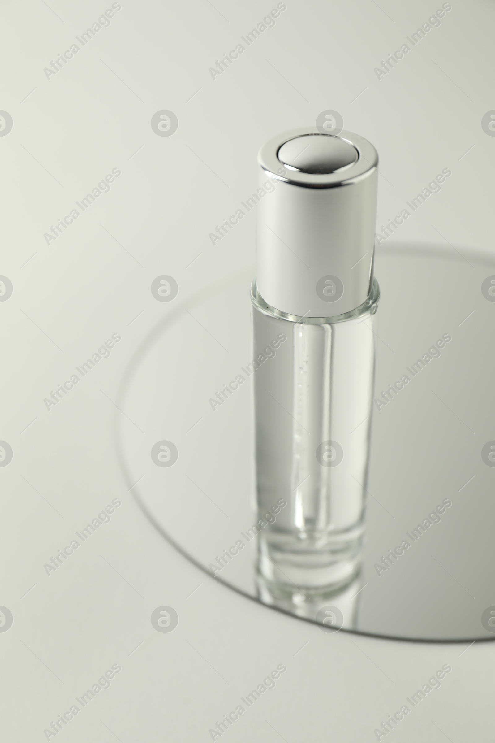 Photo of Bottle of serum and mirror on light background, closeup