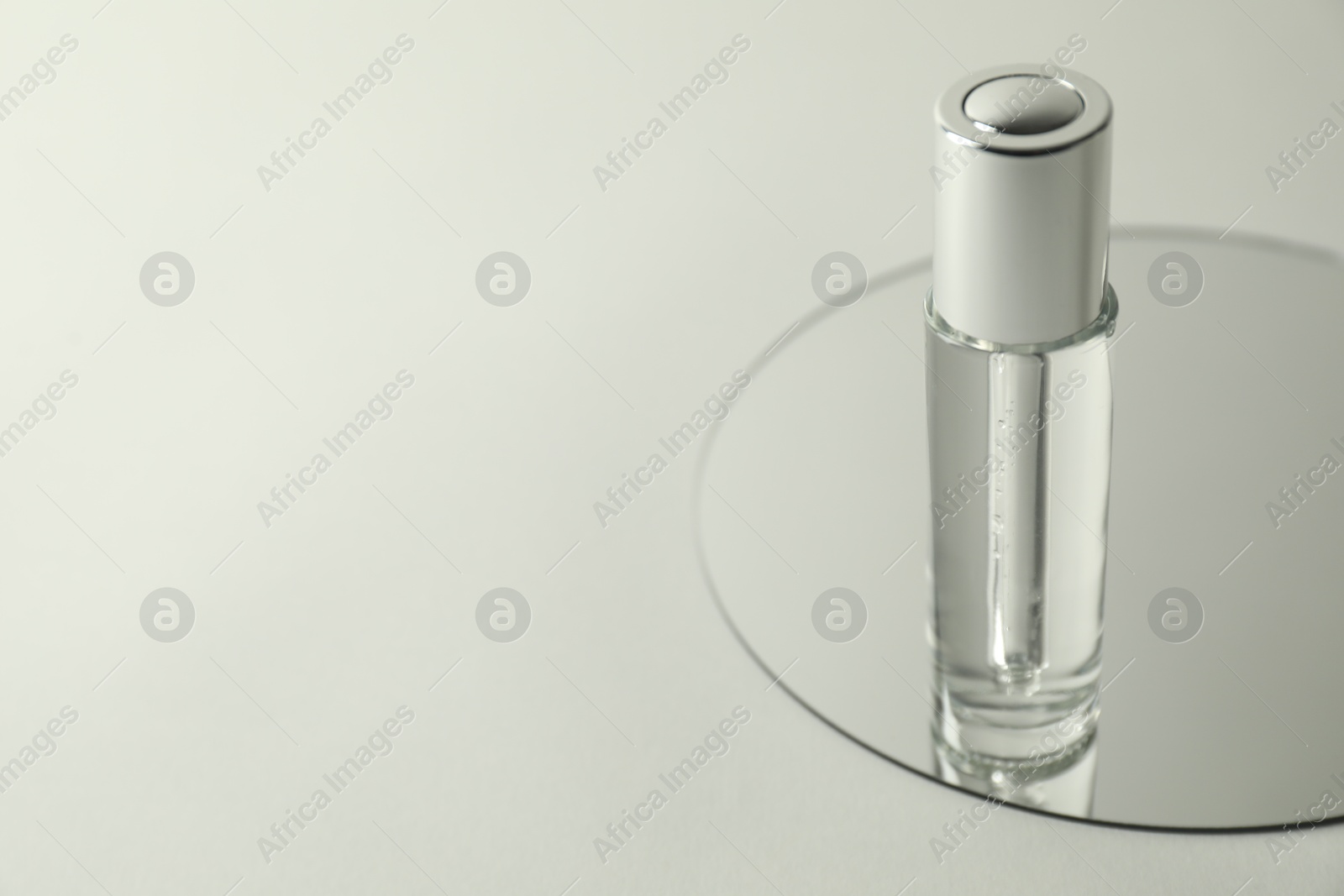 Photo of Bottle of serum and mirror on light background, space for text