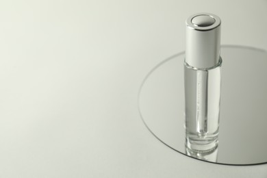 Photo of Bottle of serum and mirror on light background, space for text