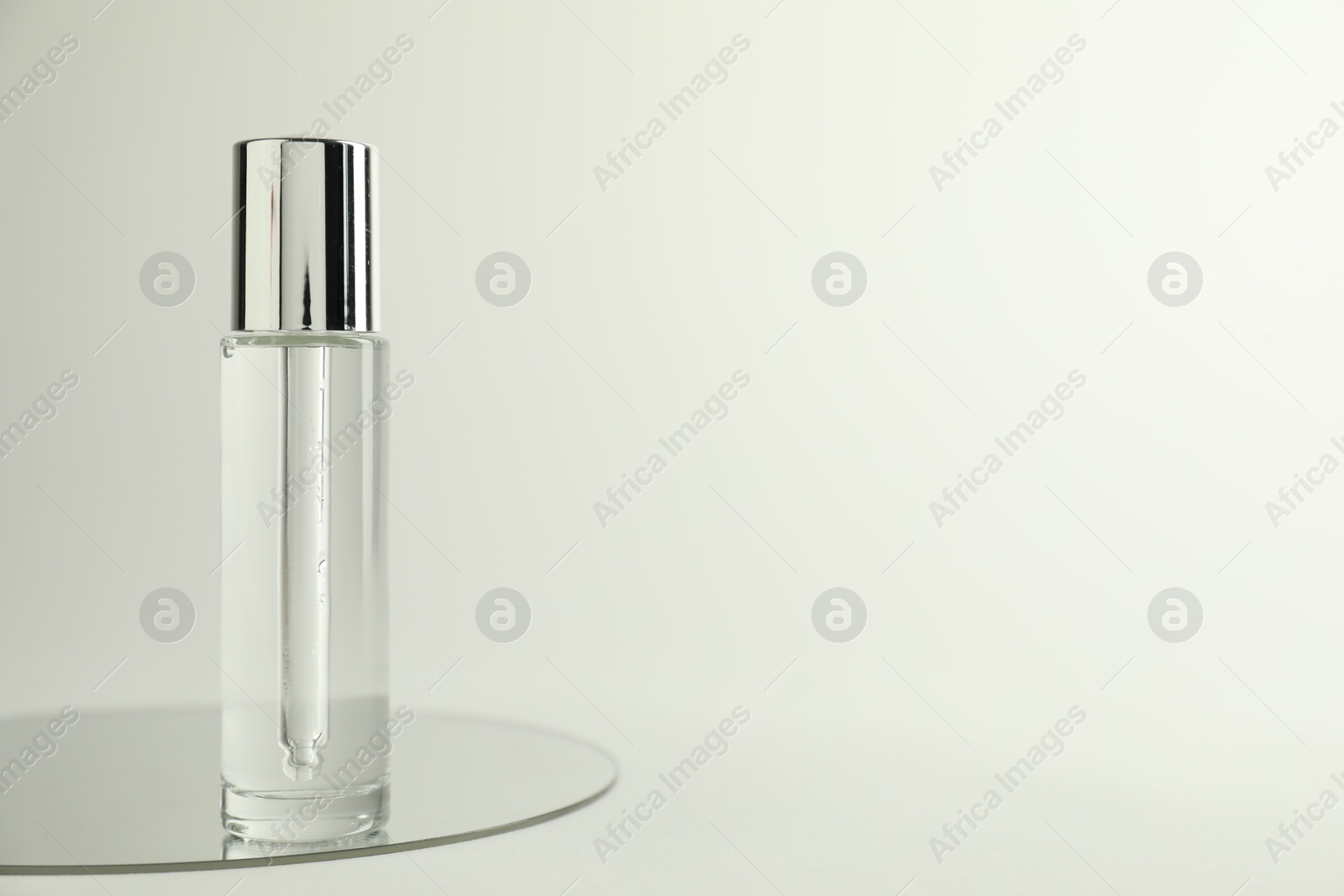 Photo of Bottle of serum and mirror on light background, space for text