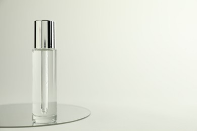 Photo of Bottle of serum and mirror on light background, space for text