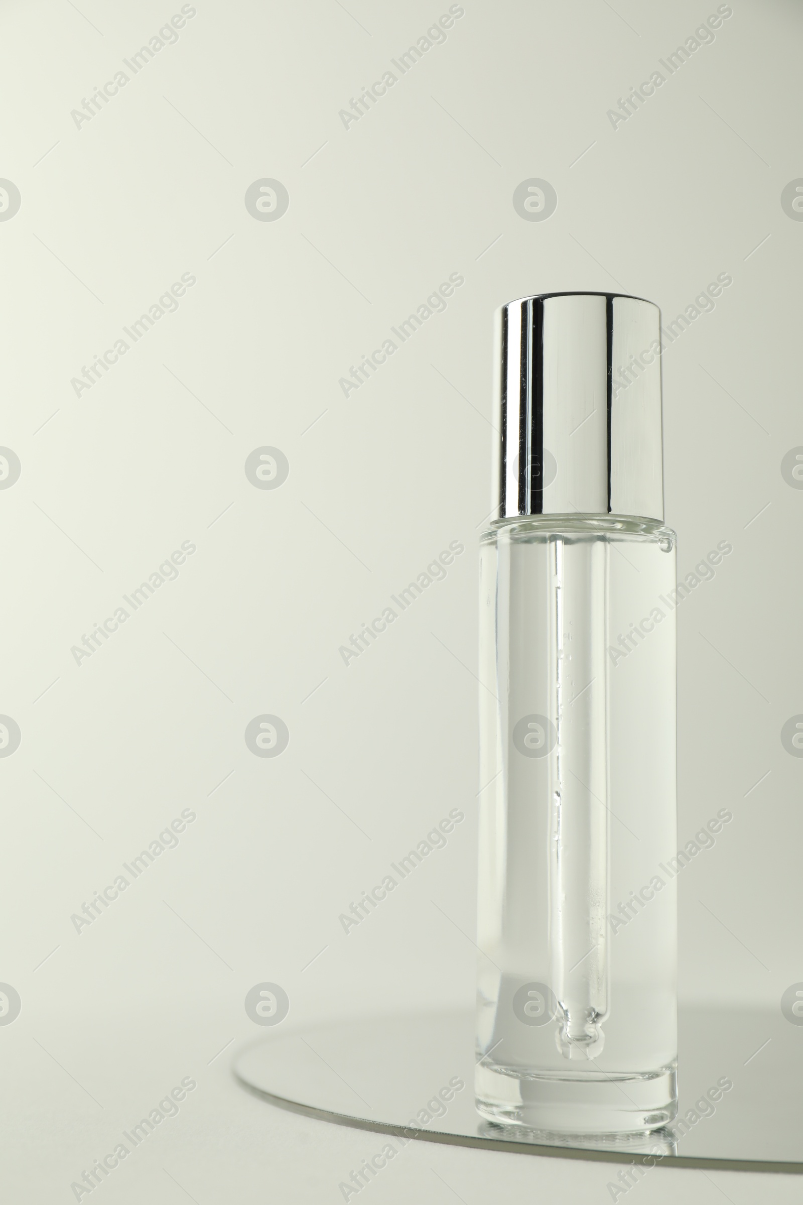 Photo of Bottle of serum and mirror on light background, space for text