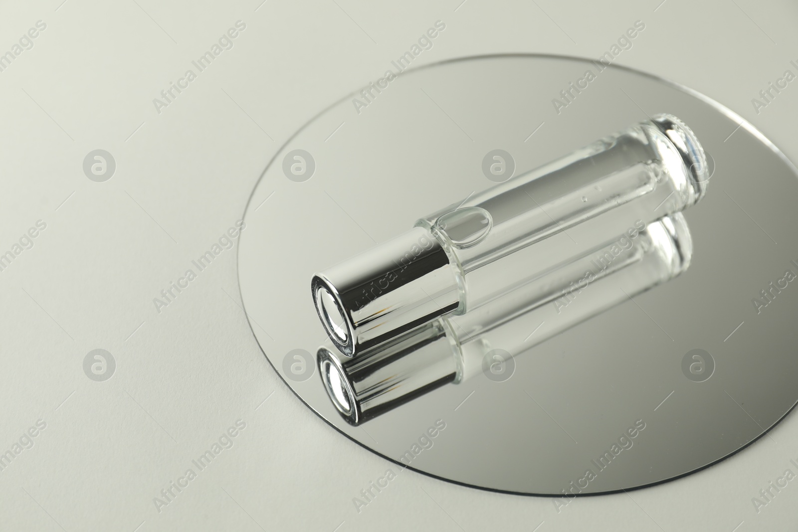 Photo of Bottle of serum and mirror on light background, space for text