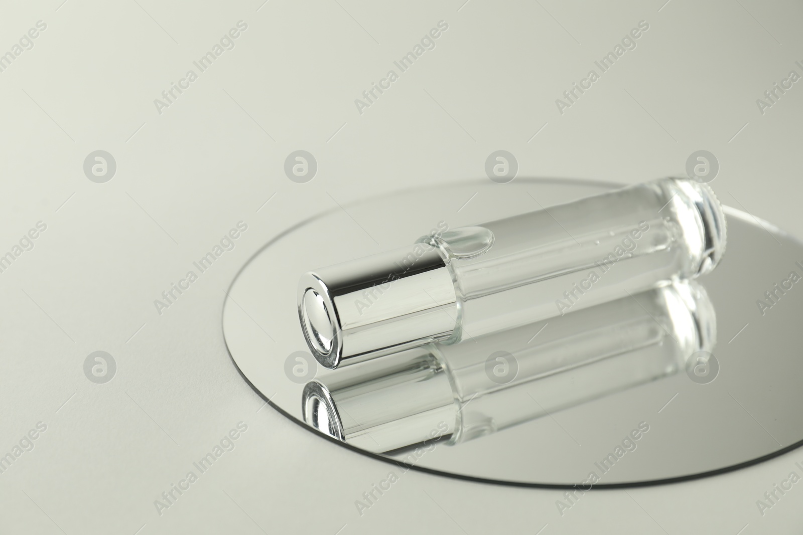 Photo of Bottle of serum and mirror on light background, space for text