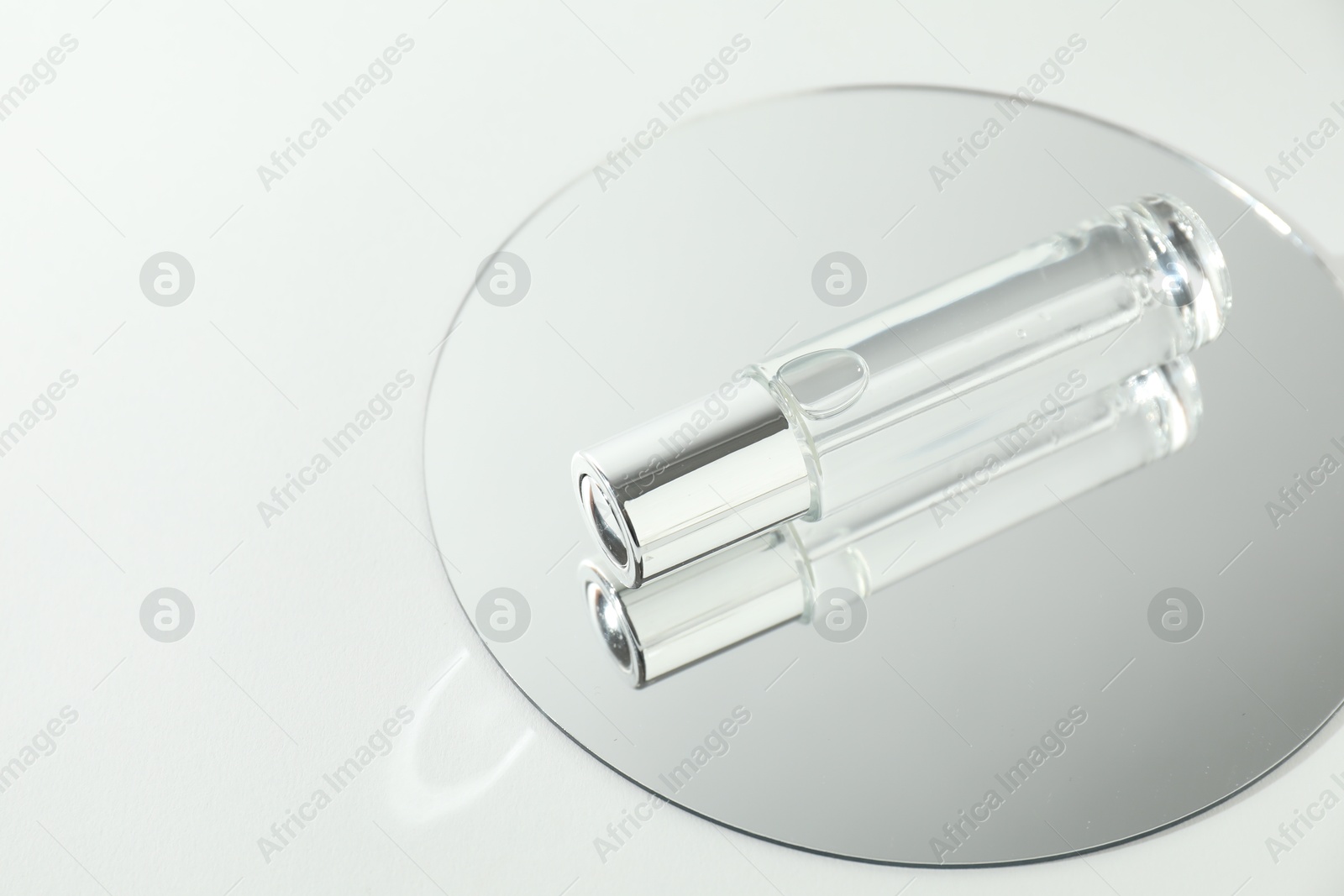 Photo of Bottle of serum and mirror on light background, space for text