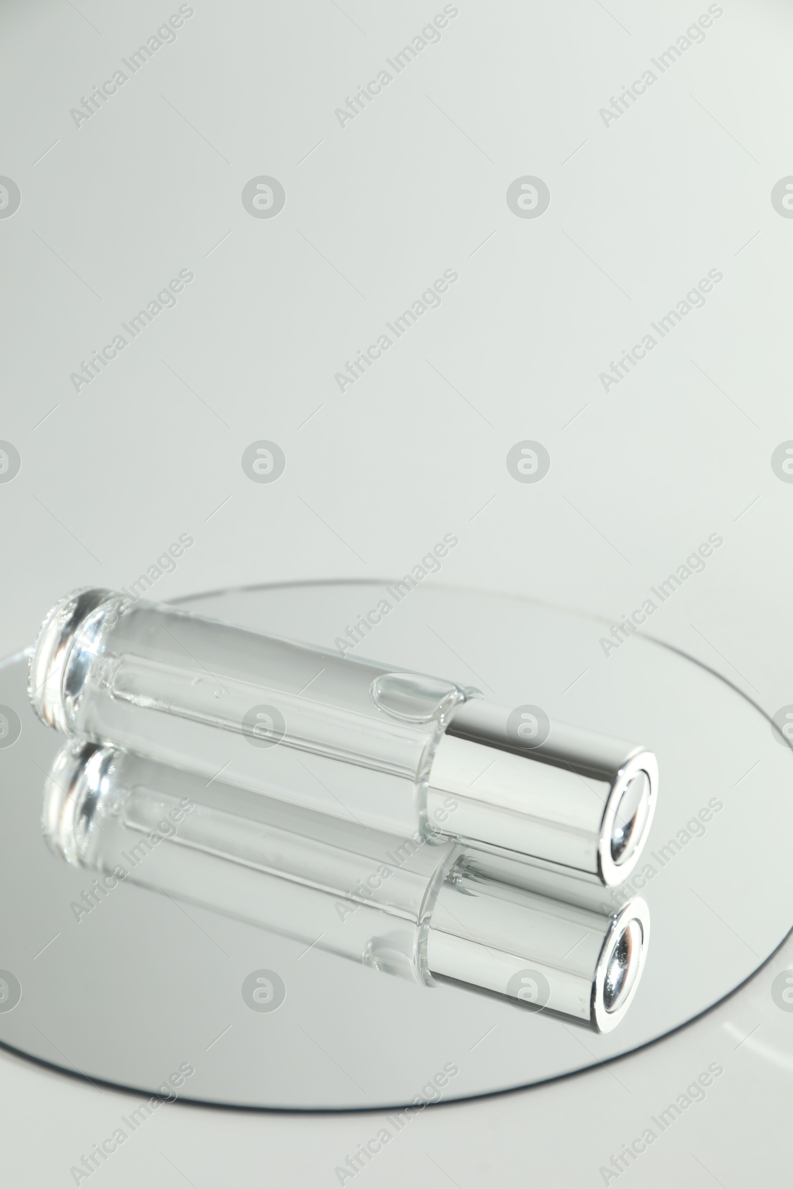 Photo of Bottle of serum and mirror on light background, space for text